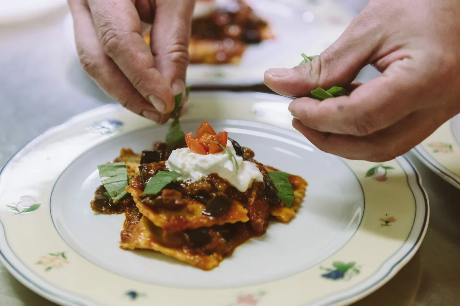Le mani che completano un piatto di pasta con una foglia di basilico